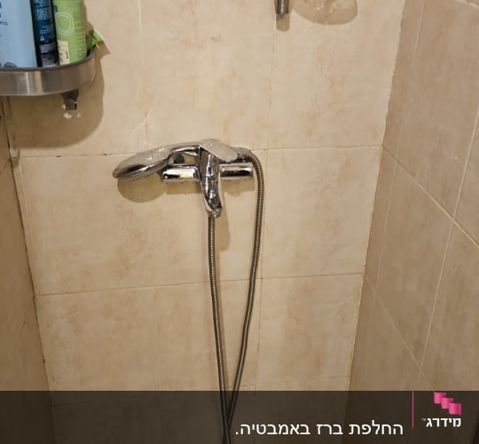 ברז מקלחת עם צינור מתכת על קיר אריחים